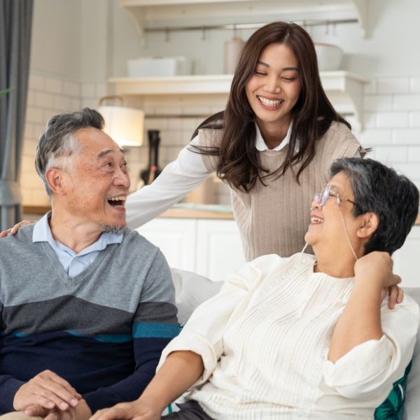 Adult daughter spending quality time laughing with elderly parents at home